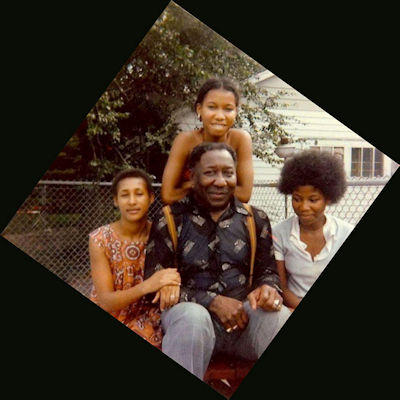 Muddy Waters at his [1974-1983] home, 16 South Adams St. in Westmont, Illinois, 1978; l to r: Muddy Waters with (l to r) his wife Marva and his daughters Mercy and Renee in front of his home, 16 South Adams St. in Westmont, Illinois; source: Internet; photographer's name not given