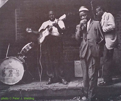 'Huston Phillip''s drum, J O H N N Y   Y O U N G, Big John Wrencher & Carey Bell at the corner of 14th and Newberry St., Chicago, IL; source: Back cover of Testament T-2203 (re-release by OJL 19??) 'Modern Chicago Blues'; photographer: Peter J. Welding